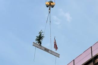 The last beam of the Pritchard Building project is hoisted by a crane with a fir tree and an American flag resting on it.