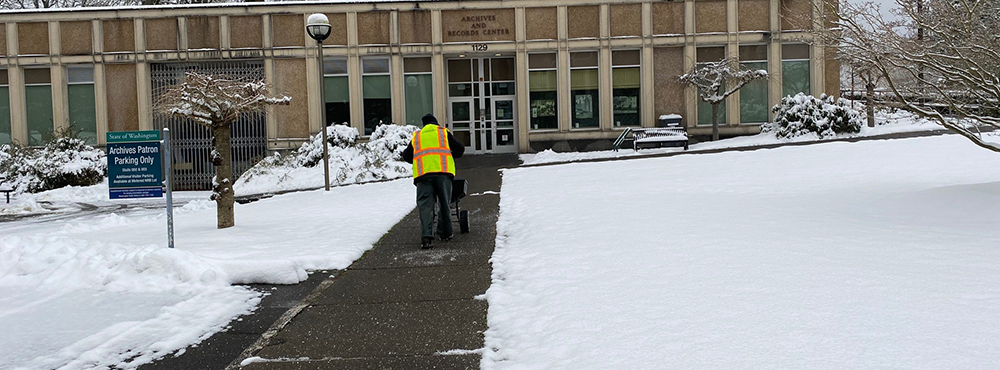 A DES employee spreads ice melt on the sidewalk in front of the State Archives Building.